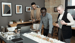 Two people look on while a third presents an architectural design