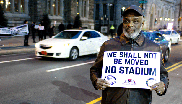 An older man holds a sign in protest of plans for a new stadium