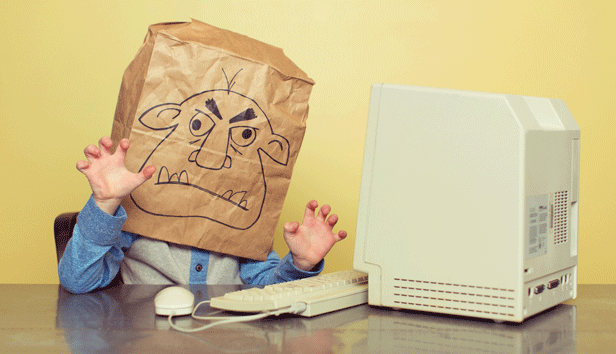 A person sitting in front of a computer with a bag over their head decorated with a picture of a troll