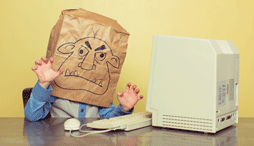 A person sitting in front of a computer with a bag over their head decorated with a picture of a troll