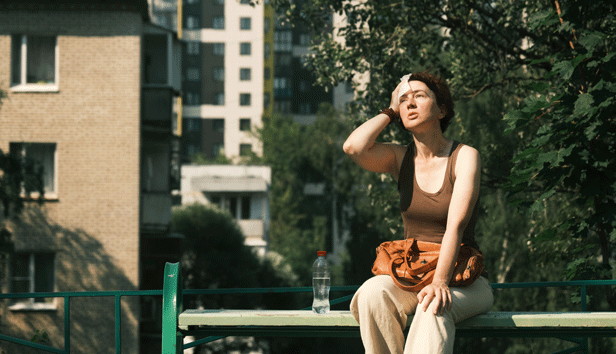 A woman sits on a bench in the hot sun