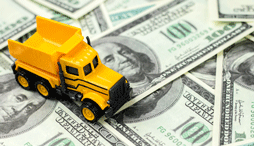 Yellow toy dump truck on dollar bills background