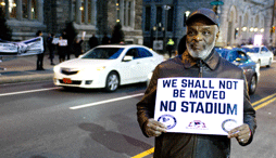 An older man holds a sign in protest of plans for a new stadium