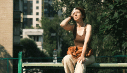 A woman sits on a bench in the hot sun